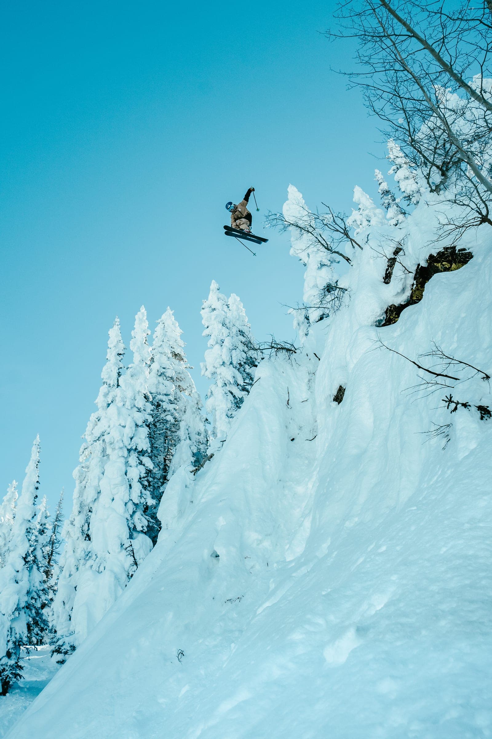 Snowboarder launching off a rime-coated cliff into cyan sky